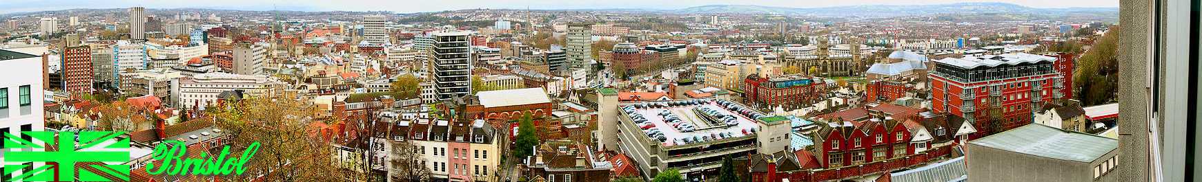 A panoramic view looking over a
cityscape of office blocks, old
buildings, church spires and a
multi-story car park. In the distance
hills.